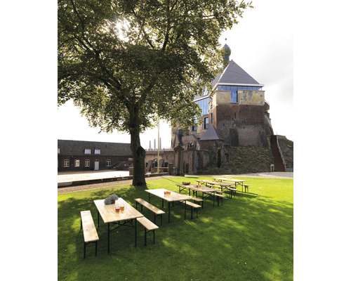 Vy med bordar och bänkar på en gräsmatta framför en historisk byggnad