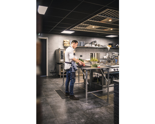 En kock förbereder mat i ett professionellt kök på en arbetsbänk i rostfritt stål.