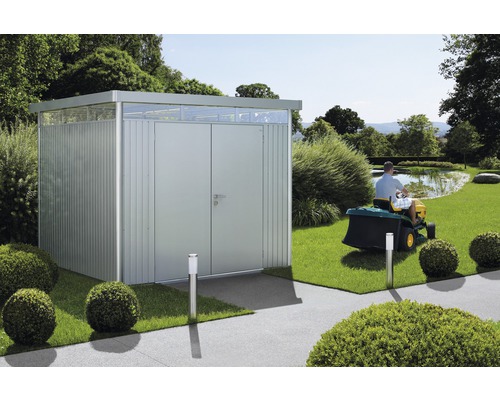 Trädgårdsbod i metall med dubbeldörr och takfönster i en trädgård med åkgräsklippare