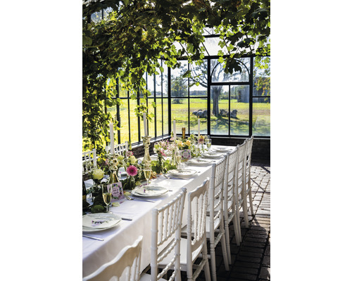 Festligt dukat bord med vita stolar i ett växthus för en fest