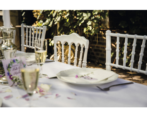 Festligt dukat bord med vita stolar, glas och dekorationer för en utomhusfest.