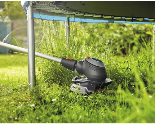 Grästrimmer i drift under en studsmatta i trädgården.