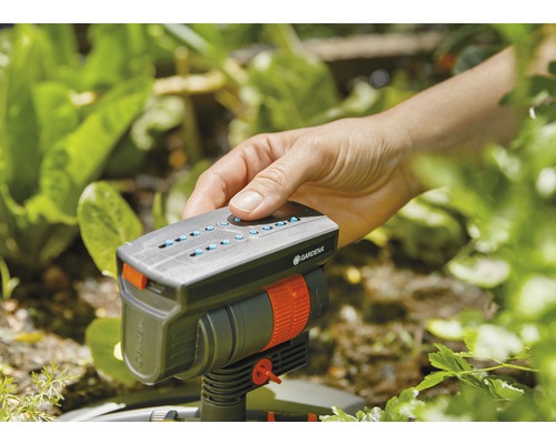 En hand använder en Gardena-bevattnare i trädgården.