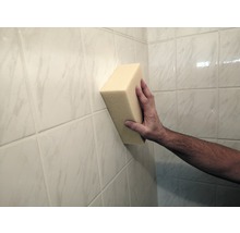 En hand håller en svamp mot en kakelvägg.