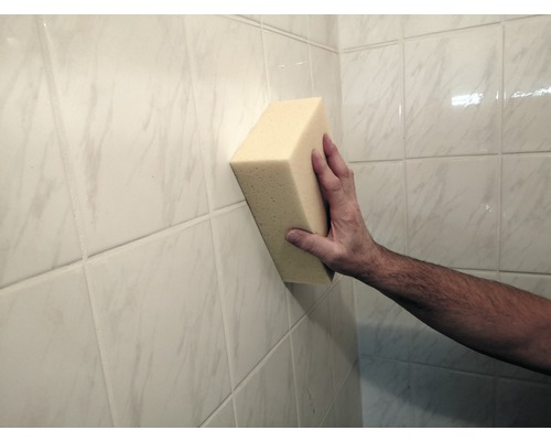 En hand håller en svamp mot en kakelvägg.