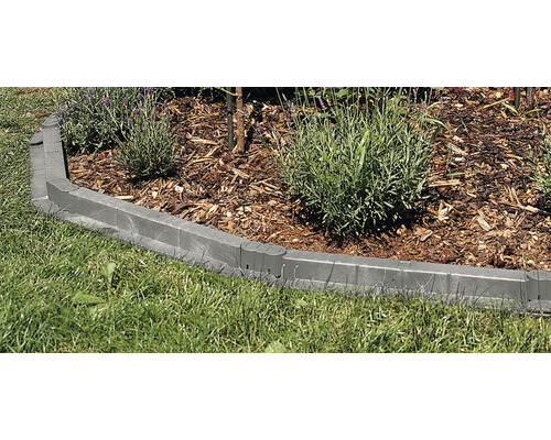 Trädgårdslandskap med gräsmatta och en rabatt omgiven av en gräsmattekant av plast.