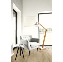 Ljust vardagsrum med fåtölj, golvlampa och litet bord på trägolv