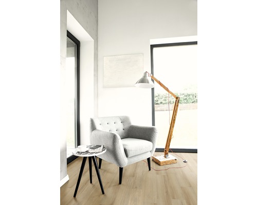 Ljust vardagsrum med fåtölj, golvlampa och litet bord på trägolv