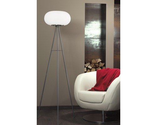 Golvlampa med stativ och rund lampa i ett vardagsrum med fåtölj och ved.