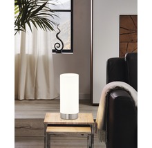 Miljöbild med en cylinderformad bordslampa i glas och metall på ett träbord