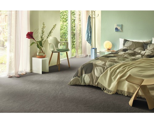 Modernt sovrum med grå heltäckningsmatta, säng med mönstrade sängkläder och vita sängbord.