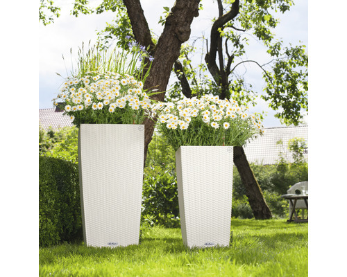 Två höga planteringskärl med flätstruktur och plantering i trädgården.