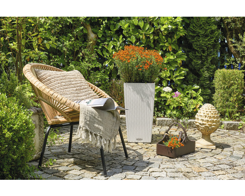 Trädgårdsscen med rottingfåtölj, blomlåda och dekoration på stengolv