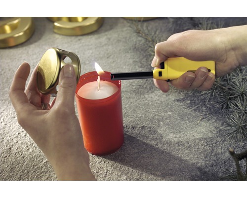 En person tänder ett ljus med en tändare. Bredvid ljuset ligger ett ljuslock.