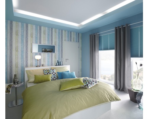 Ljust sovrum med dubbelsäng, mönstrad tapet och fönster med gardiner och persienner