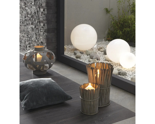 Dekorativ scen med lykta, kudde, vindljus av kvistar och trädgårdskulor på grus