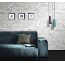 Vardagsrum med soffa, kudde, bilder och taklampor framför en mönstrad tegelvägg