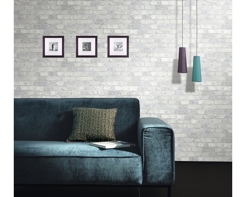 Vardagsrum med soffa, kudde, bilder och taklampor framför en mönstrad tegelvägg