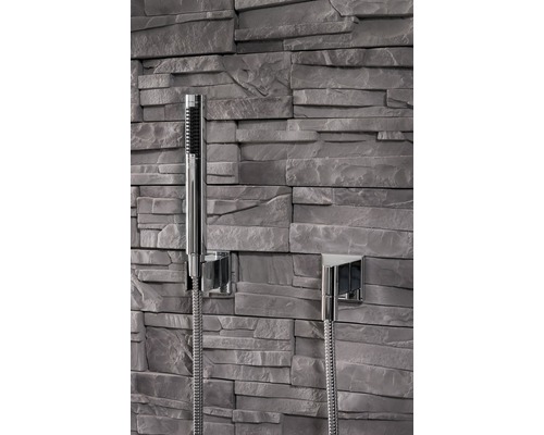 Handdusch med duschslang framför stenmur