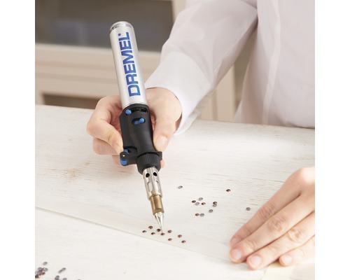 En person använder en Dremel-brännare för att fästa strassstenar på ett band.