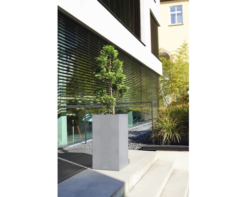 Grå blomlåda med växt på en utomhustrappa framför en byggnad.