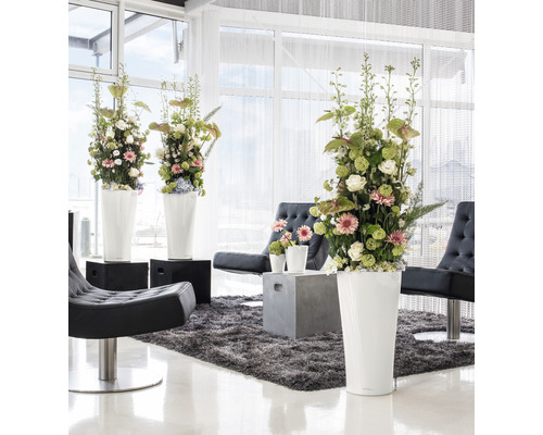 Ljus inredning med blomsterarrangemang i höga blomkrukor, fåtöljer och matta