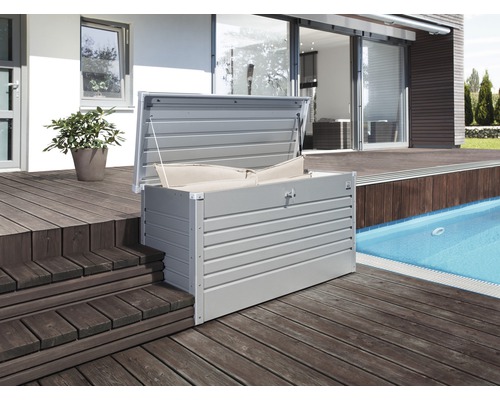 Öppen förvaringslåda i metall med kuddar på en träterrass bredvid en pool