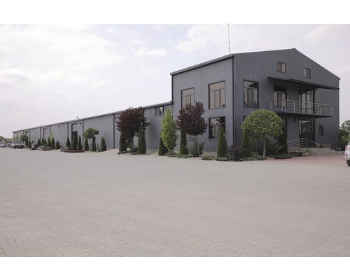 Exteriör av en stor industribyggnad med parkeringsplats och träd