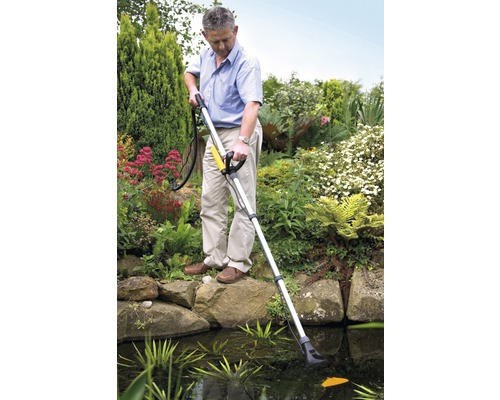 Man rengör trädgårdsdamm med dammsugare för damm mot en trädgårdsscen