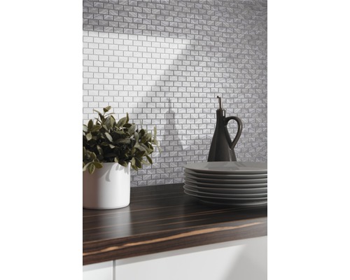 Köksscen med kakel i tegelstensutseende, växt, tallrikar och oljeflaska på en mörk arbetsbänk.