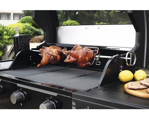 Gasolgrill med två stekta kycklingar på ett roterande spett och citroner på en träplatta