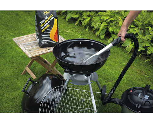 Scen med kolgrill, säck med kol och asksugare på gräsmatta