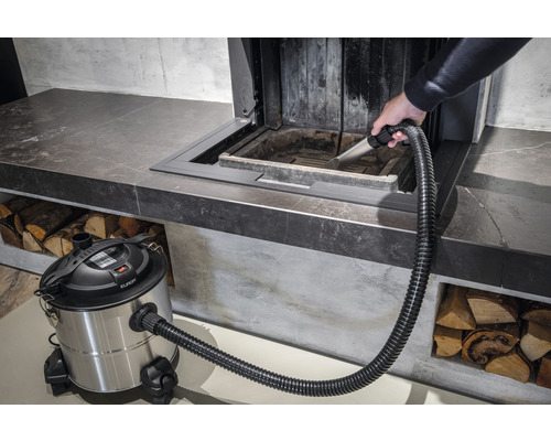 En person rengör en öppen spis med en asksugare.
