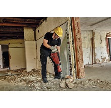 En man med skyddsglasögon och skyddshjälm arbetar med en rivningshammare i ett rum som behöver renoveras.