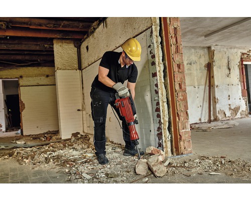 En man med skyddsglasögon och skyddshjälm arbetar med en rivningshammare i ett rum som behöver renoveras.