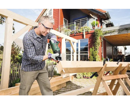 Man sågar trä med tigersåg utomhus. Träkonstruktion under uppbyggnad.