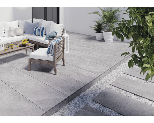 Terrass med grå plattor, trädgårdsmöbler och växter.