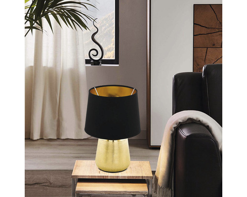 Dekorativ bordslampa med svart lampskärm och gyllene bas på ett sidobord