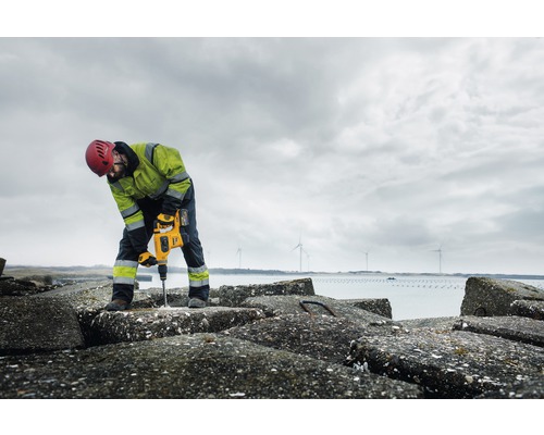 En byggnadsarbetare borrar med en borrhammare i betongblock vid vattnet.