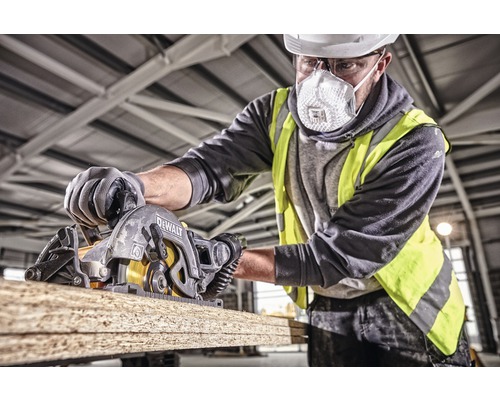 Man med skyddshjälm, skyddsglasögon och andningsmask sågar en bräda med en DeWalt cirkelsåg.