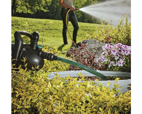 Trädgård med trädgårdspump, slang och en person som vattnar med en trädgårdsslang