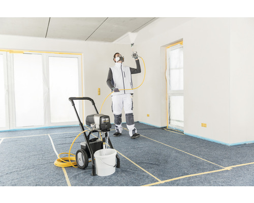 En man använder en färgspruta i ett täckt rum för målningsarbeten.