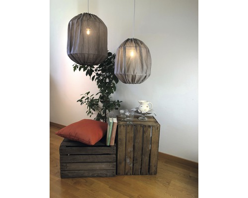 Två tyglampor hänger i ett rum ovanför en dekoration av växter, kuddar och trälådor.