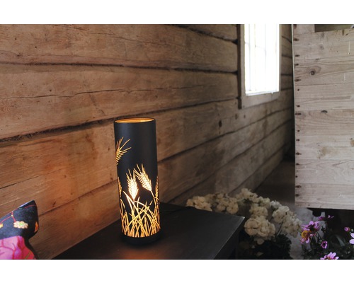 Dekorativ bordslampa med veteaxmönster på ett nattduksbord i ett rustikt rum.