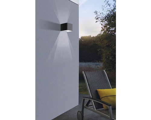 Kubisk utomhusvägglampa av metall med ljuskägla på husväggen