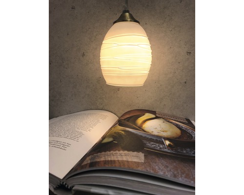 Hängande lampa med glasskärm ovanför en öppen bok.