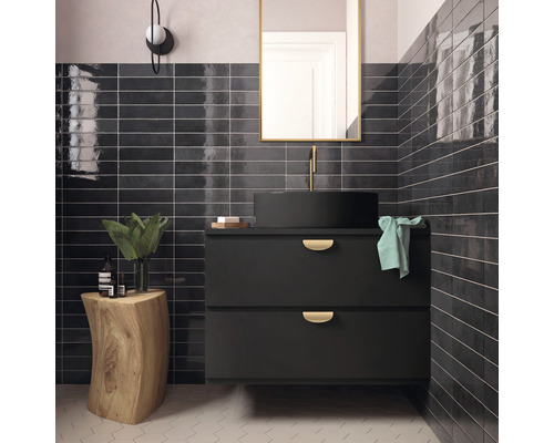 Badrum med svart tvättställsskåp, runt handfat, rektangulär spegel och svarta glänsande kakelplattor