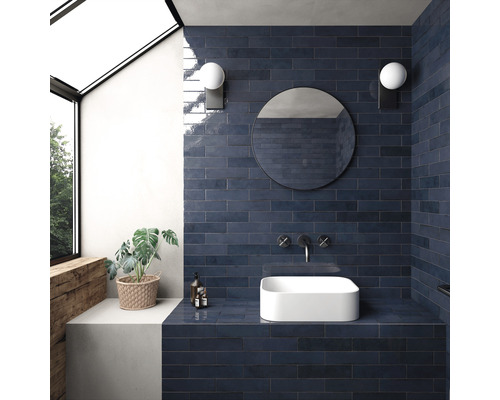 Badrum med blått kakel, tvättställsskål, spegel och vägglampor