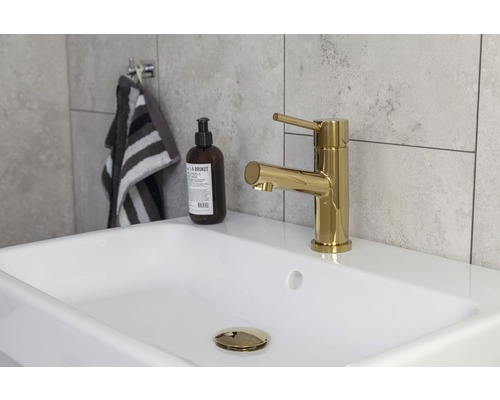 Bild av ett tvättställ med guldfärgad armatur, tvålpump och handduk