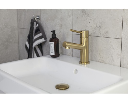 Detaljvy av ett badrum med handfat, en gyllene kran, handtvål och en handduk